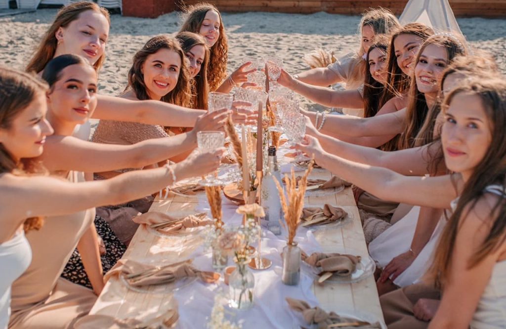 Uczestniczki wieczoru panieńskiego wznoszą toast przy piknikowym stole na plaży