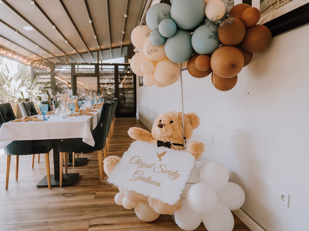 Dekoracja z okazji chrzcin: miś z balonami przy udekorowanym stole jadalnym