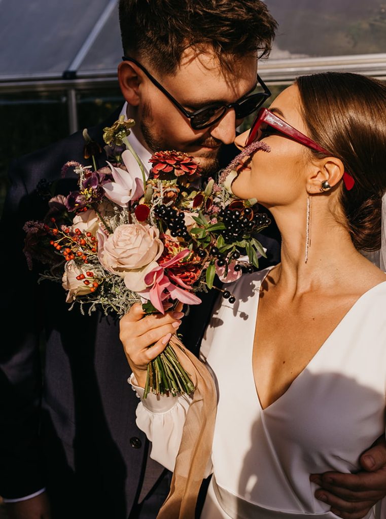 Panna młoda i pan młody całujący się. Panna młoda trzyma bukiet kwiatów w dłoni.
