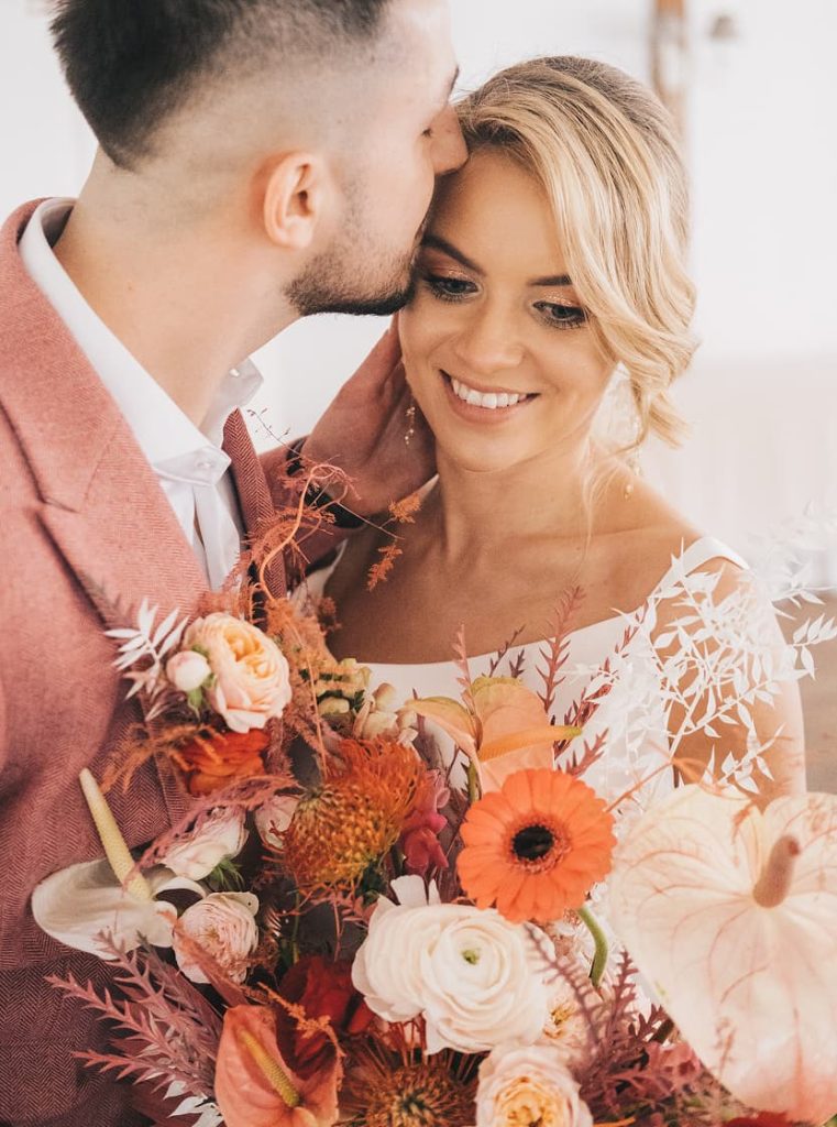 Pan młody całuje panną młodą trzymającą kolorowy bukiet kwiatów