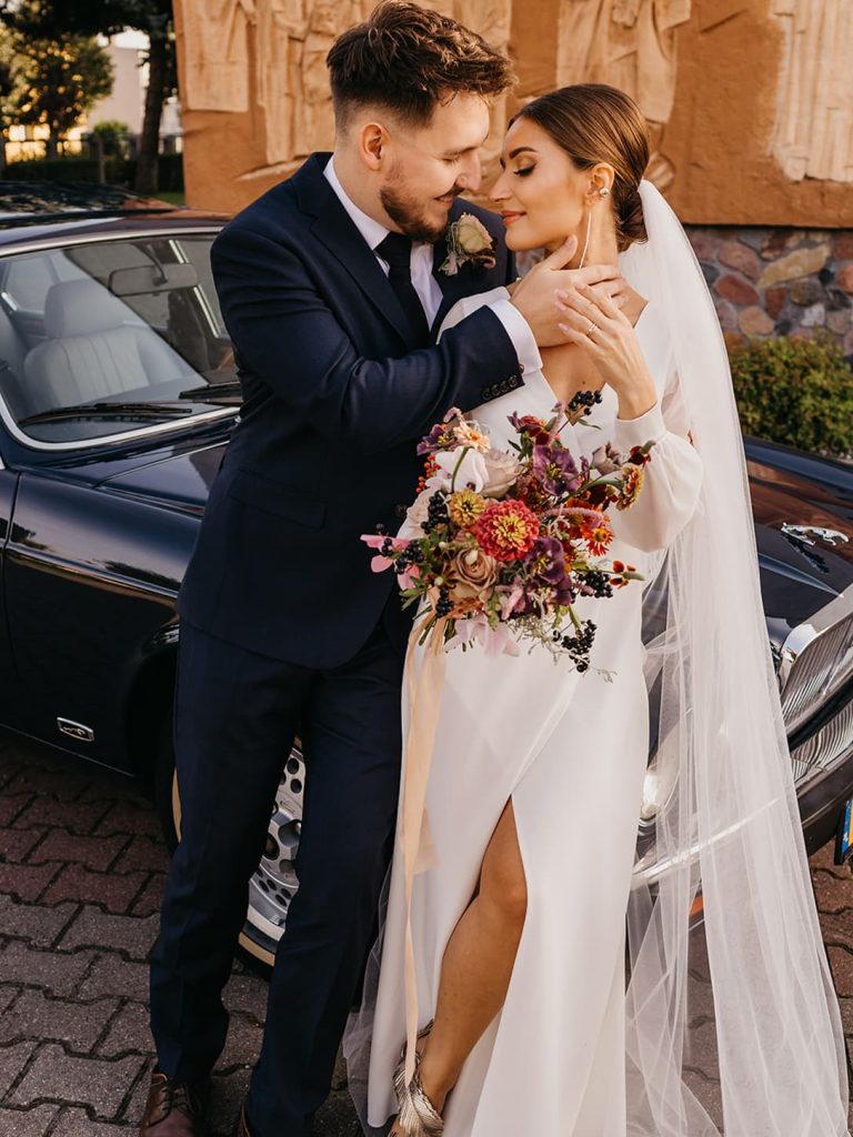 Panna młoda i pan młody obejmujący się w pobliżu eleganckiego zabytkowego samochodu