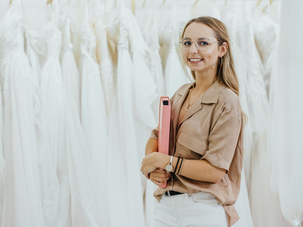 Uśmiechnięta Wedding Plannerka trzymająca teczkę w salonie sukien ślubnych